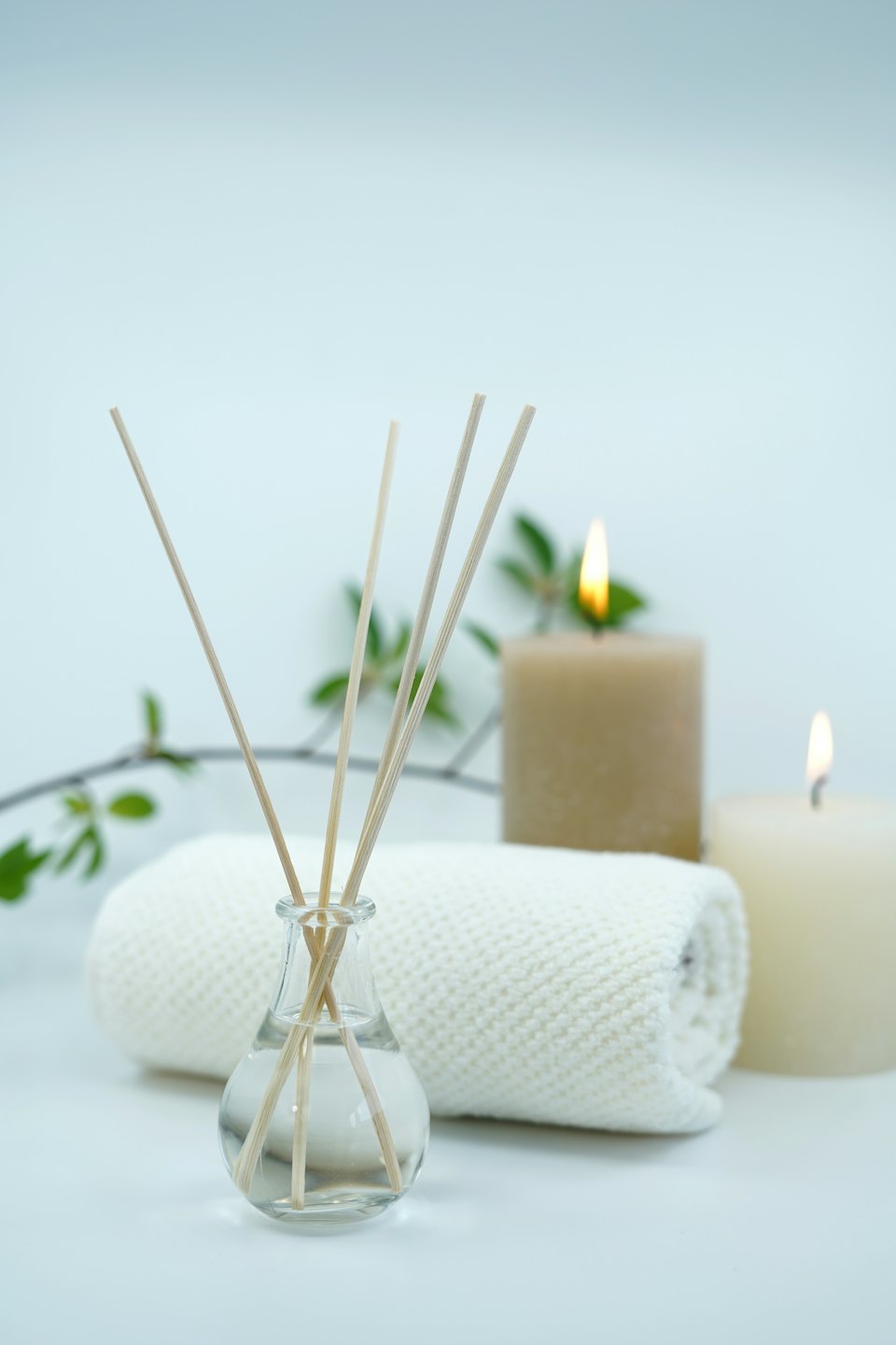 Schilfrohrdiffusor, gerolltes Handtuch und brennende Kerzen für Wellness.